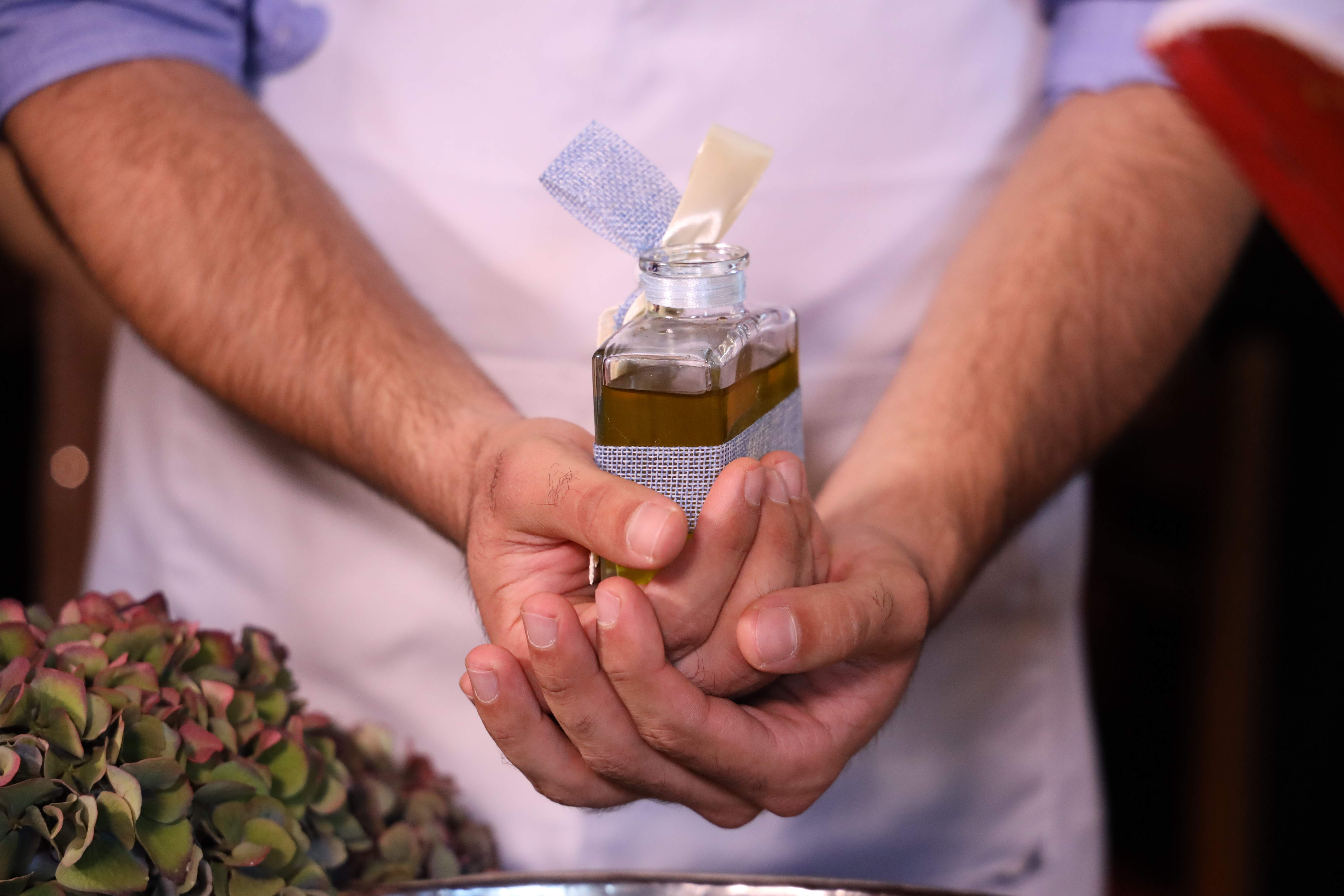 Μπομπονιέρα βάπτισης, χέρια που κρατούν διακοσμητικό μπουκαλάκι ελαιόλαδου με μπλε κορδέλα