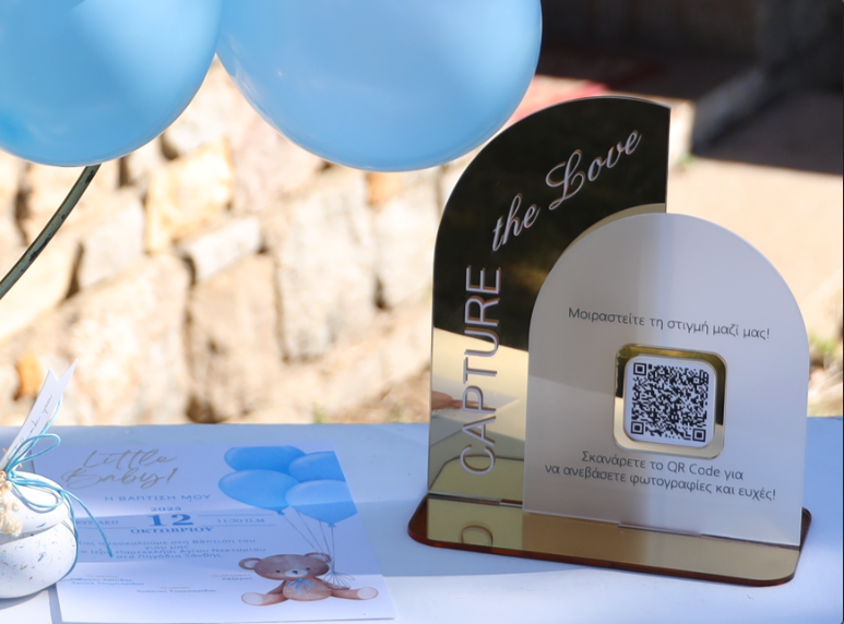 Το QR stand του Wishbook με την επιγραφή Capture the Love δίπλα στη βαπτιστική πρόσκληση και μπλε μπαλόνια